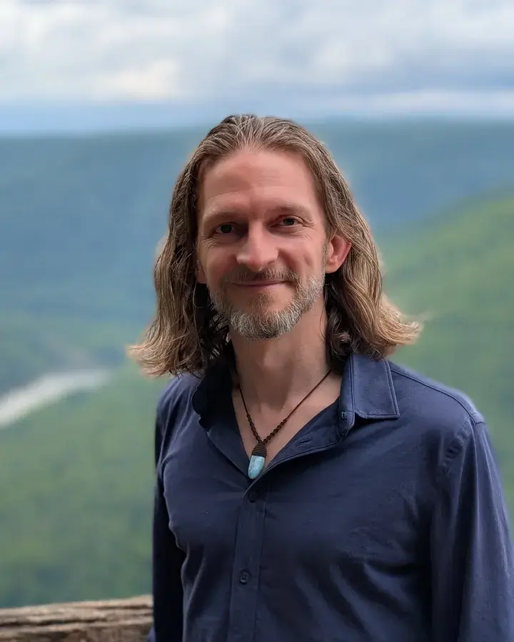 Brandon smiling at a mountain overlook, with a river valley behind