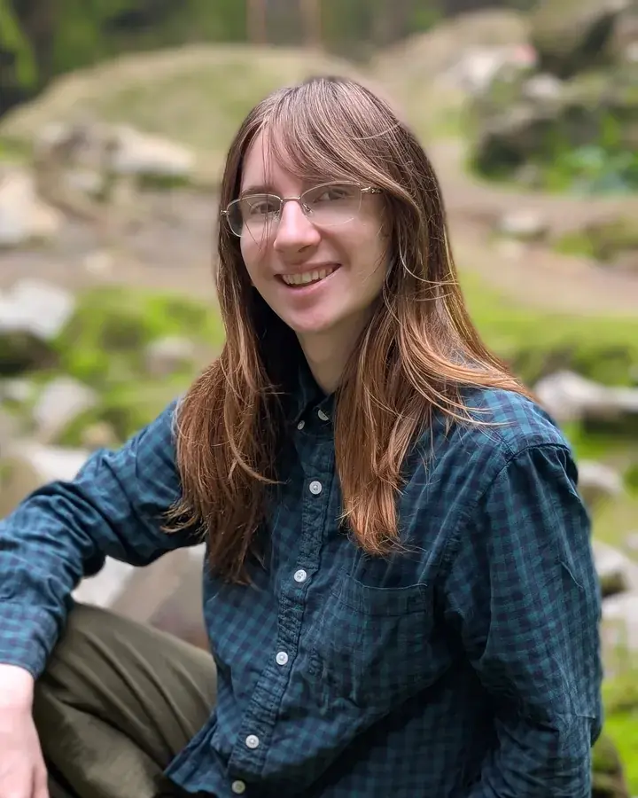 Emrys smiling, seated on a mossy rock in the woods